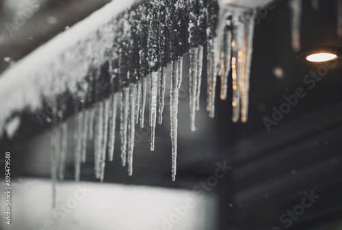Icicles hang on the roof of a house. Spring landscape with icicles hanging from the roof of the house. Set of snow icicles, snow hat. Soft focus on ice icicle photo