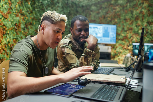 Young confident female officer of surveillance center explaining something to male colleague while sitting in front of laptop screen