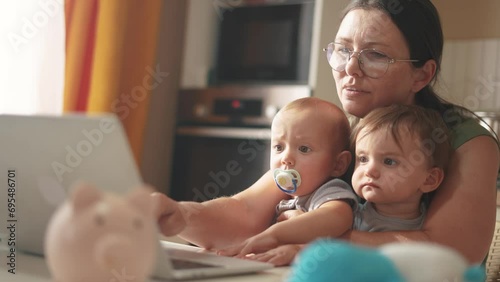 mother works remotely from home with two babies in her arms. pandemic remote work concept. mom tries to work at home in a fun kitchen, small children interfere with business sitting in her arms photo