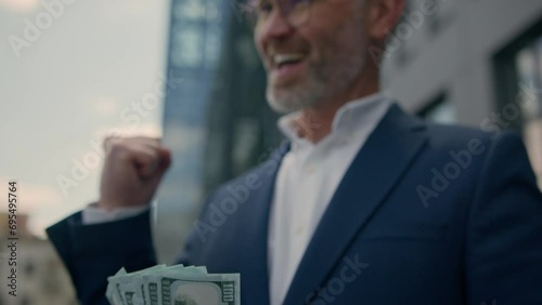 Excited happy rich old male businessman financial achievement lucky successful mature senior man employer business achieve prize holding cash money banknotes dollars winning victory gesture in city photo