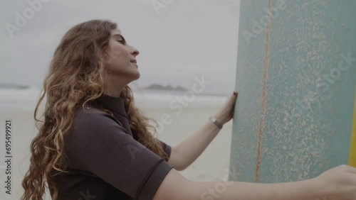 Young woman on the beach, concentrated, applying paraffin to her surfboard. Cinematic 4k. photo