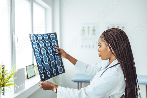 Confident female doctor sitting at office desk and examining a patient's x-ray, she is looking at X-ray. Female doctor looking at X-Ray radiography scan in patient room