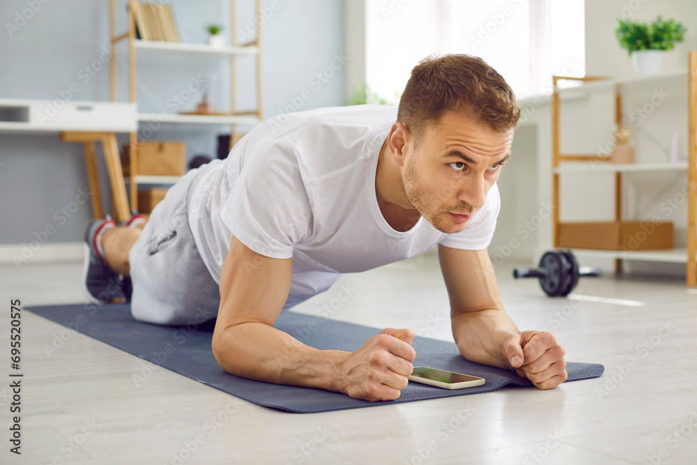 Portrait of a young attractive sporty man doing plank sport exercise lying on yoga mat on the floor in the living room at home. Fitness, fit, workout sport and home training concept.