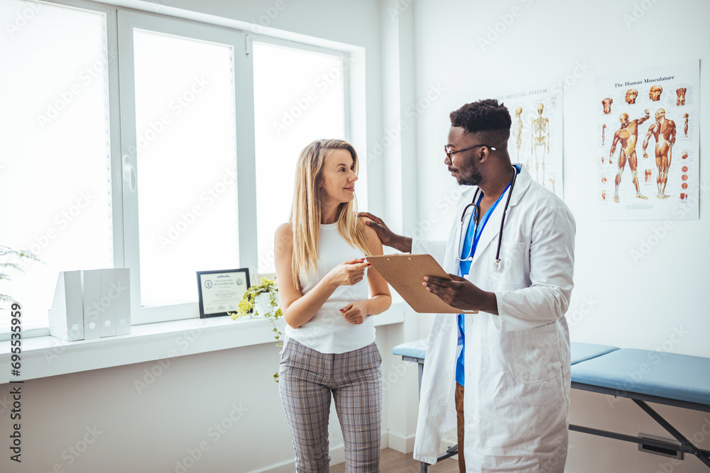 Happy young African American doctor therapist in white coat has appointment consulting supporting putting hand on shoulder of  female patient in modern clinic hospital. Medical healthcare concept.