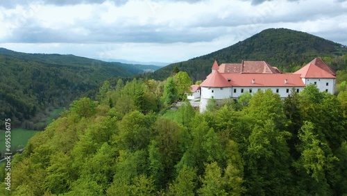 Aerial shot of quaint Turjak Castle nestled among lush green hills from fairy tale, forest, trees, Standing tall against a cloudy sky and overlooking a Valley.