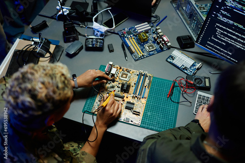 Above angle of young female officer in military uniform repairing motherboard with transmission device next to male colleague photo