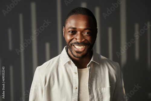 Front view portrait of carefree adult African American man smiling at camera with light and shadow background