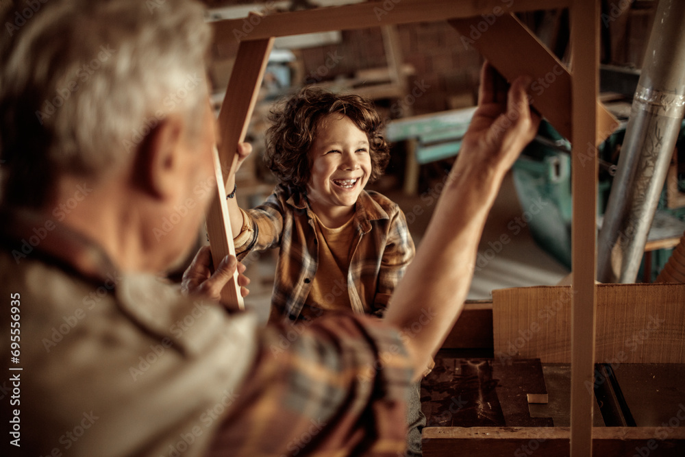 Elderly carpenter making wood frame with little boy in workshop