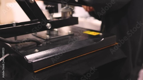Process of printing image on clothes, heat press machine printing custom design on t-shirt and hoodie in fabric workshop, screen printing shirt, textiles and clothing, lithography and serigraphy
