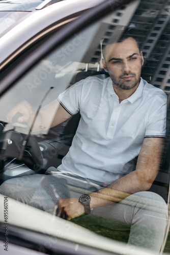 Young man in car, smiling, view through windscreen, portrait, close-up © AvokadoStudio