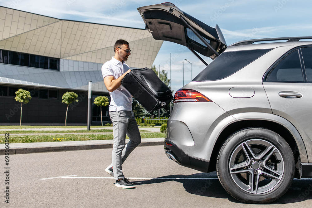 Handsome man going to vacations, loading his suitcase in car suv trunk Handsome man going to vacations, loading his suitcase in car suv trunk