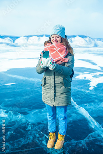 Happy smiling woman traveler online chatting on mobile phone while standing outdoors on frozen Baikal lake in winter day 