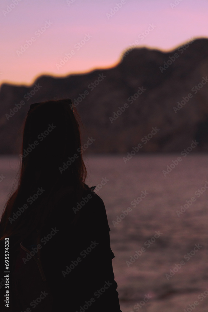 Silhouette of a woman on the left of the image overlooking an ocean sunset, vertical image