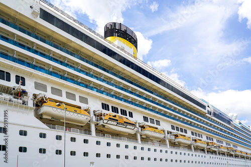 Side view of a large cruise ship with many hanging lifeboats and liferafts, blue sky background photo