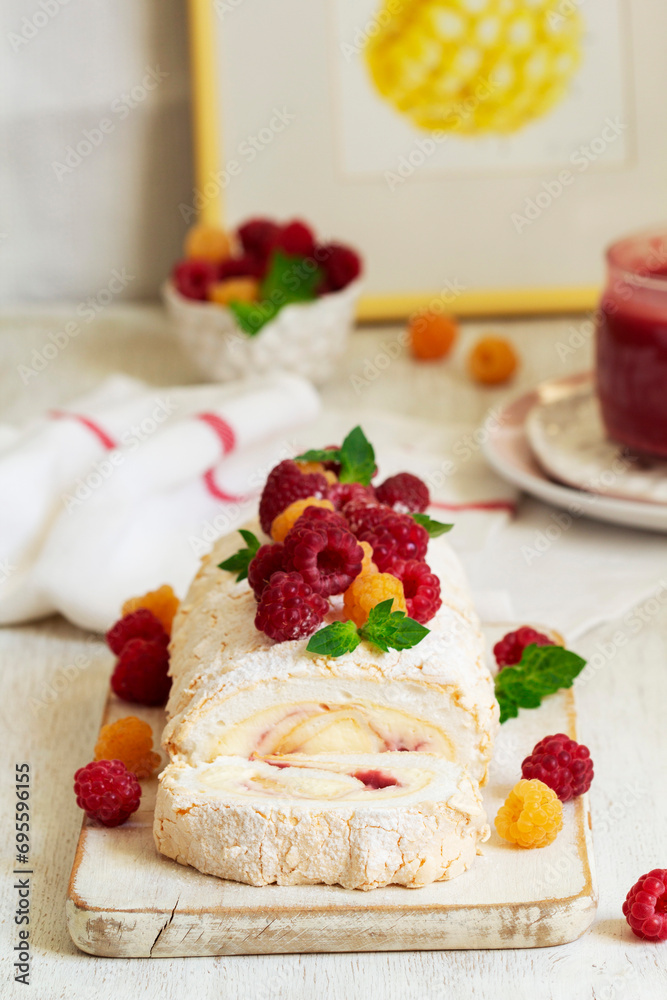 Meringue roll with butter cream and raspberry curd, decorated with berries on a light background.