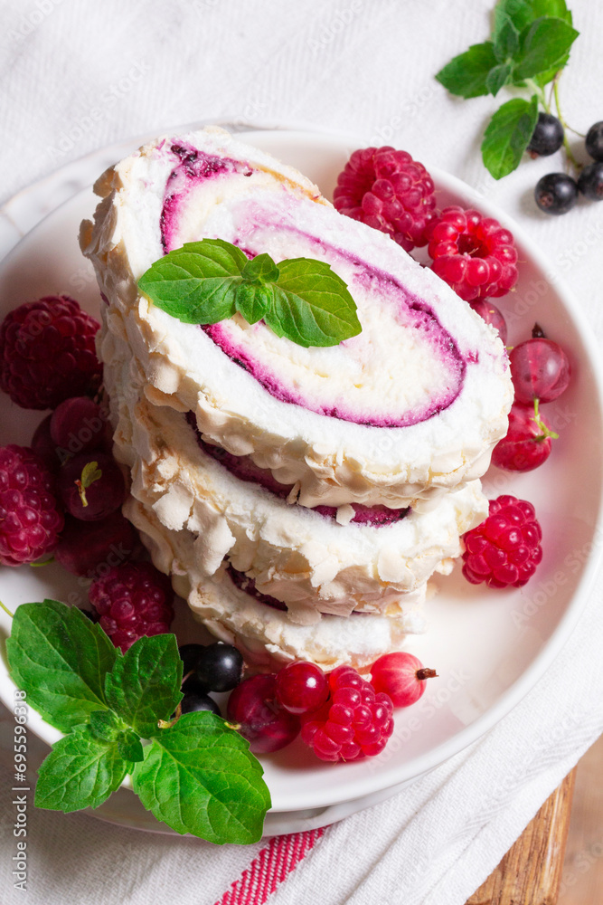 Meringue roll with whipped cream and currant curd, served with berries on a ceramic plate. Rustic style.