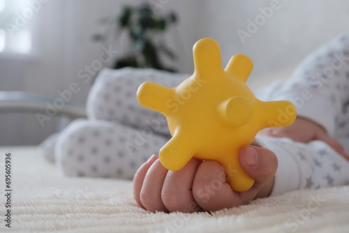 A baby is sleeping in a crib, a child of European appearance, wearing a light light jumpsuit. A yellow rubber toy in the hand. Sleep patterns for babies, care and hygiene.