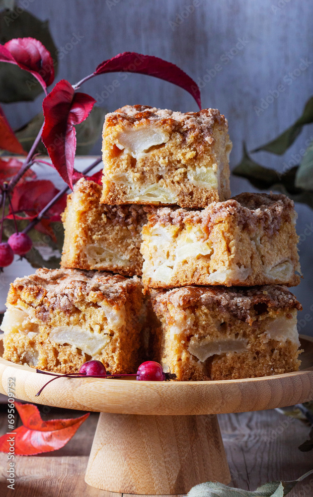 Slices of Dutch apple cake with streusel on a wooden tray, apples and apple branches on a wooden background.