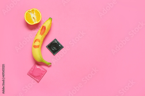 Fresh banana with lipstick kiss, orange and condoms on pink background. Sex education concept photo