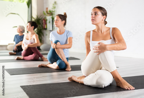 Calm European female gym visitor practicing Half Lord of the fishes pose or Ardha Matsyendrasana during group yoga training