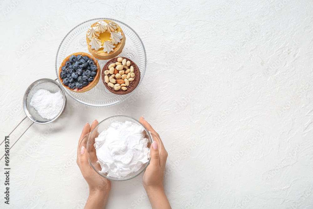 Female confectioner with bowl of whipped cream and tasty cakes on white background