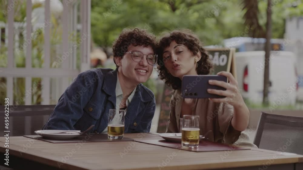 Casal de namoradas tirando uma selfie, sentado em um bar ao ar livre. Cinematico 4k.