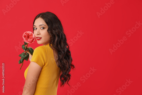 Young Asian woman with beautiful pink rose on red background