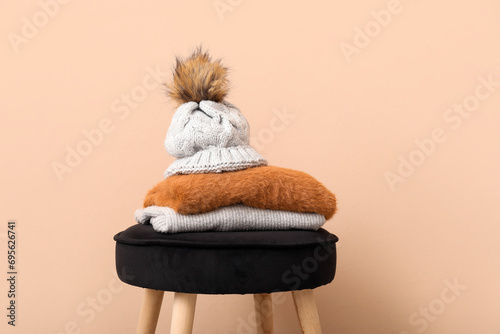 Stack of folded sweaters with hat on chair against beige background