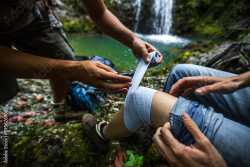 Assistance of a Woman Thigh With an Elastic Medical Bandage from First Aid Travel Kit on a Hike in Wilderness photo