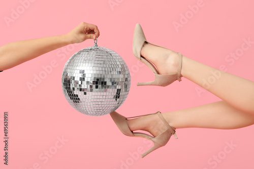 Female legs in trendy high heels and hand with disco ball on pink background photo