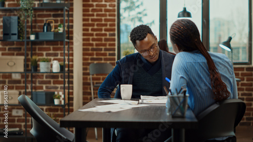 African american team analyzing papers, looking at annual data reports and reading research information on documents. Startup employees collaborating in boardroom meeting office.