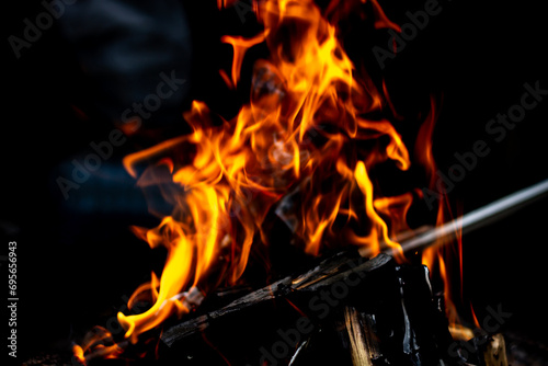 Horizontal color photo of an open fire, coals, ashes, firewood close up with a darkened black background. Selective focus on the main object.