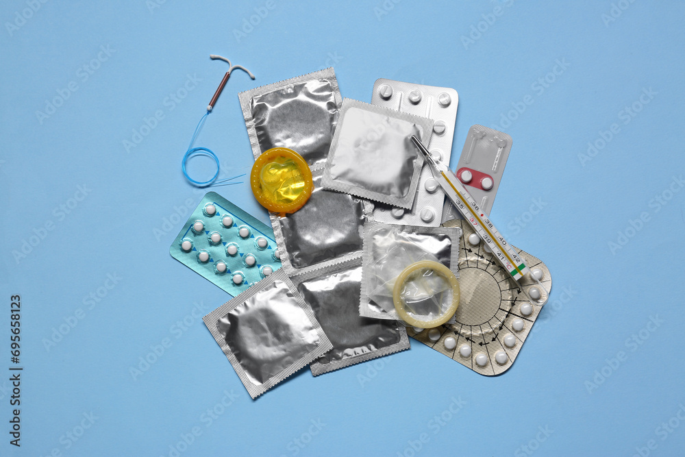 Contraceptive pills, condoms, intrauterine device and thermometer on light blue background, flat lay. Different birth control methods Contraceptive pills, condoms, intrauterine device and thermometer on light blue background, flat lay. Different birth control methods