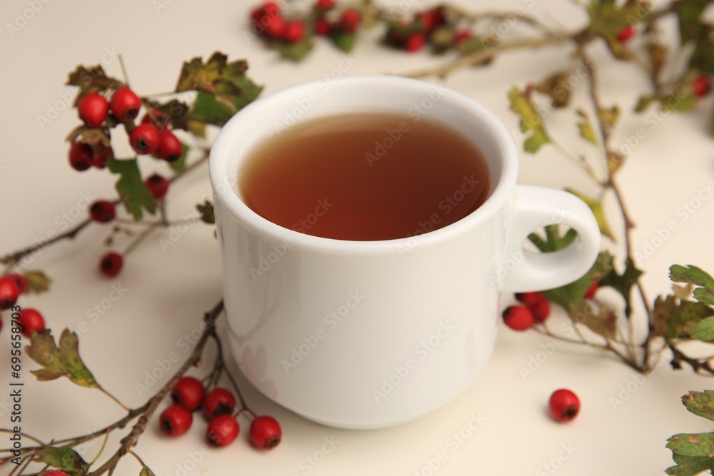 Aromatic hawthorn tea in cup and branch with berries on beige table, closeup Aromatic hawthorn tea in cup and branch with berries on beige table, closeup