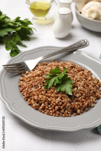 Tasty buckwheat with fresh parsley and fork on white tiled table