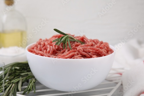 Fresh raw ground meat and rosemary in bowl on table, closeup