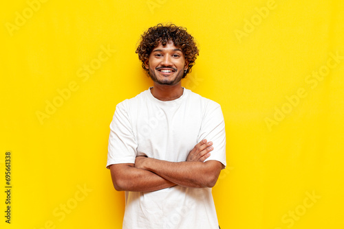 young indian curly guy standing with crossed arms over yellow isolated background and smiling