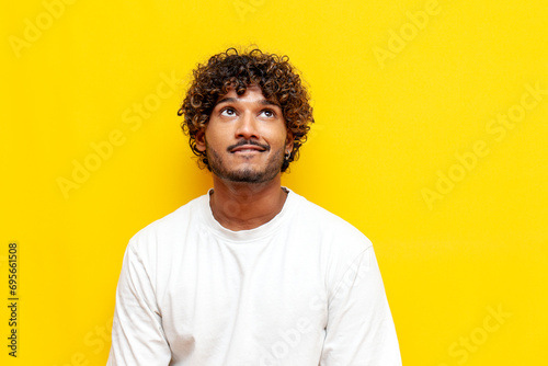 young indian excited guy hoping and waiting looking up on yellow isolated background