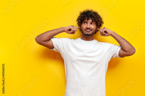 young indian guy avoids and ignores noise over yellow isolated background photo