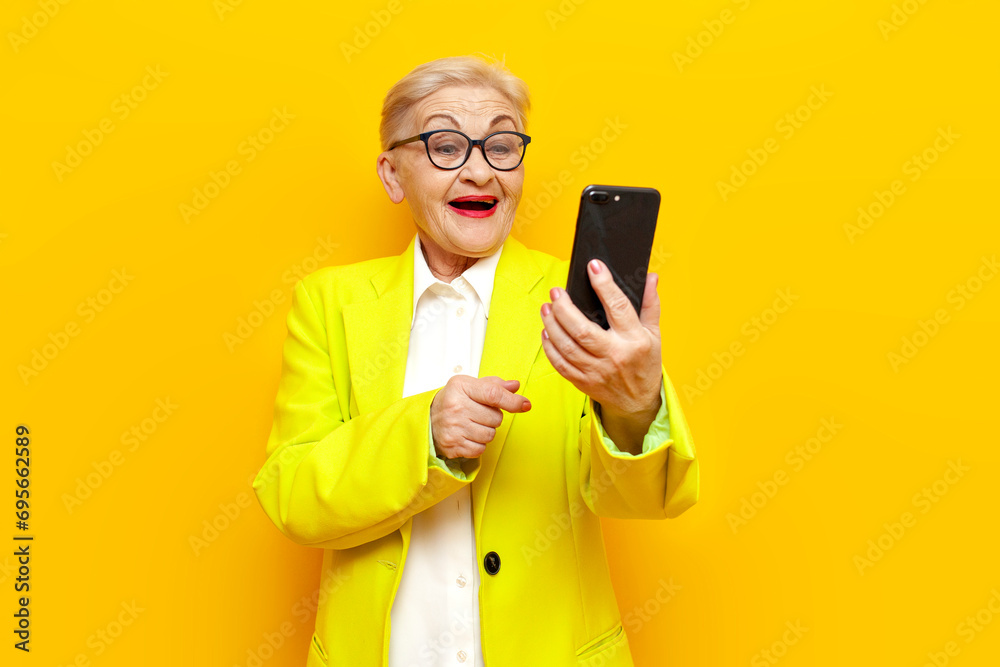 funny old business granny in blazer and glasses using smartphone online and laughing on yellow background funny old business granny in blazer and glasses using smartphone online and laughing on yellow background