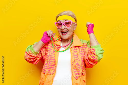 funny crazy old granny in sports hipster clothes rejoices at success and victory on a yellow isolated background photo