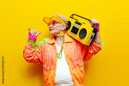 funny old granny with tape recorder in sports hipster clothes takes selfie online on yellow isolated background
