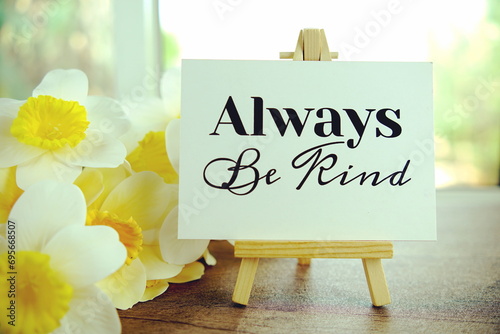 Always be kind text message on paper card with wooden easel on wooden table background, inspiration motivation concept photo