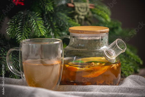 Orange fragrant tea in a glass teapot on the background of a Christmas tree. Cozy warm festive atmosphere