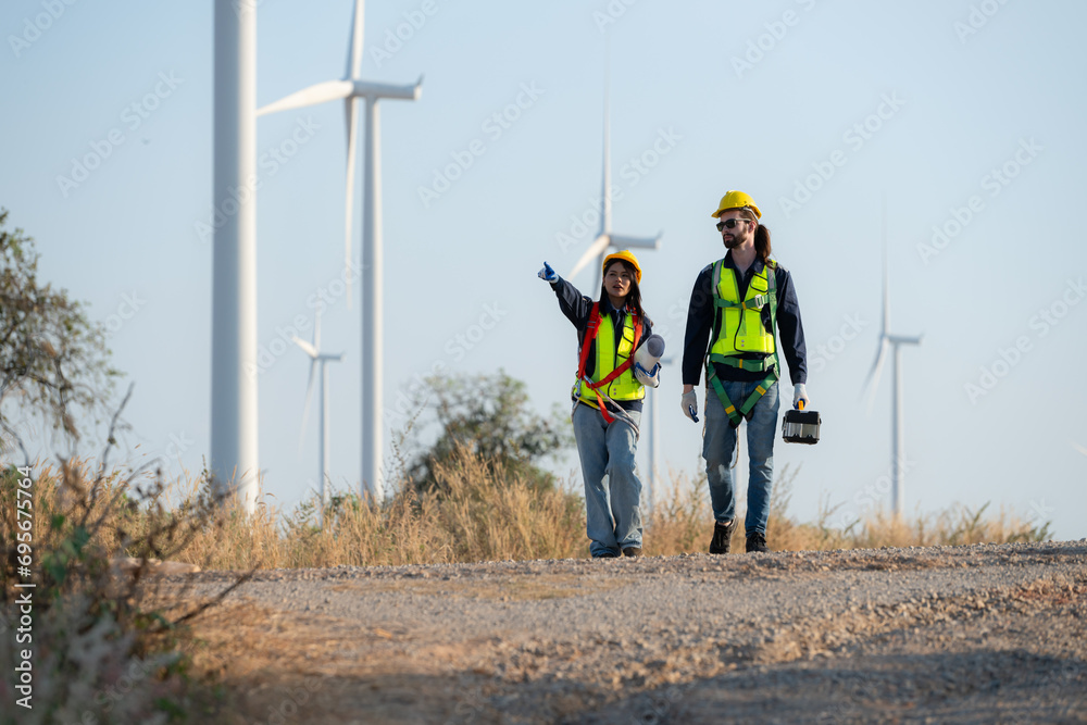 Engineer and worker discussing on a wind turbine farm with blueprints Engineer and worker discussing on a wind turbine farm with blueprints