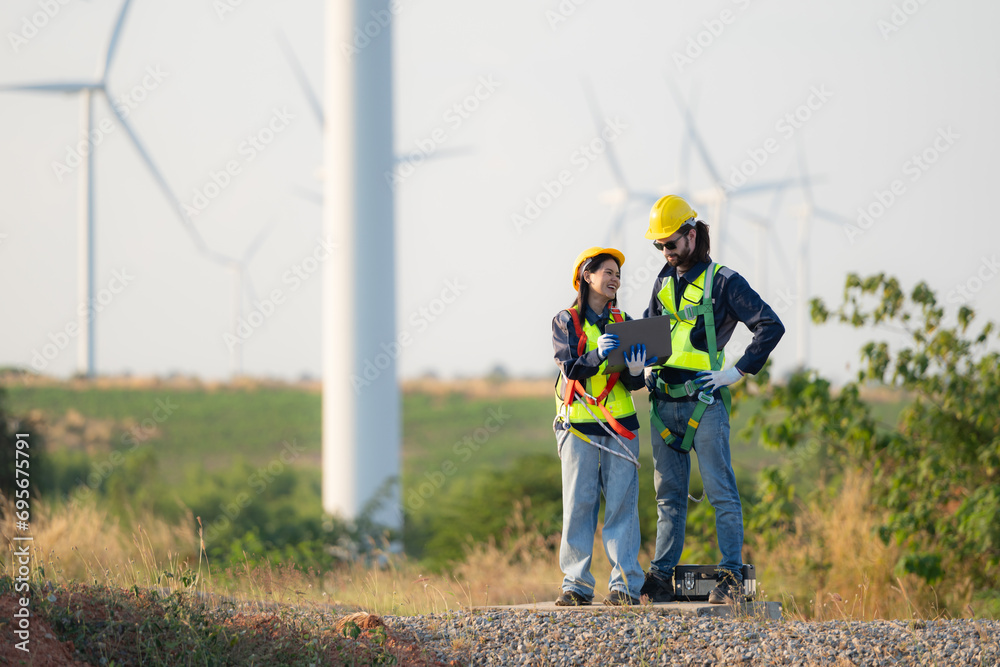 Engineer and worker discussing on a wind turbine farm with blueprints Engineer and worker discussing on a wind turbine farm with blueprints