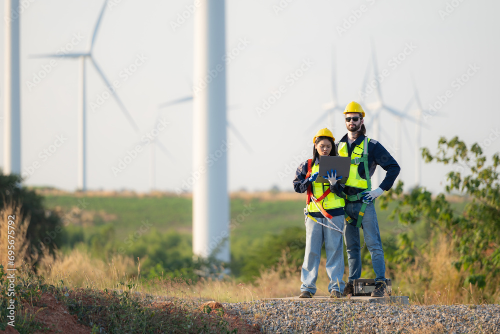 Engineer and worker discussing on a wind turbine farm with blueprints Engineer and worker discussing on a wind turbine farm with blueprints