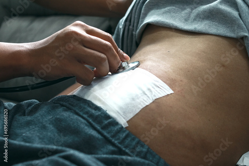 Doctor's hand using stethoscope checking patient stomach in the clinic, post appendectomy surgery photo