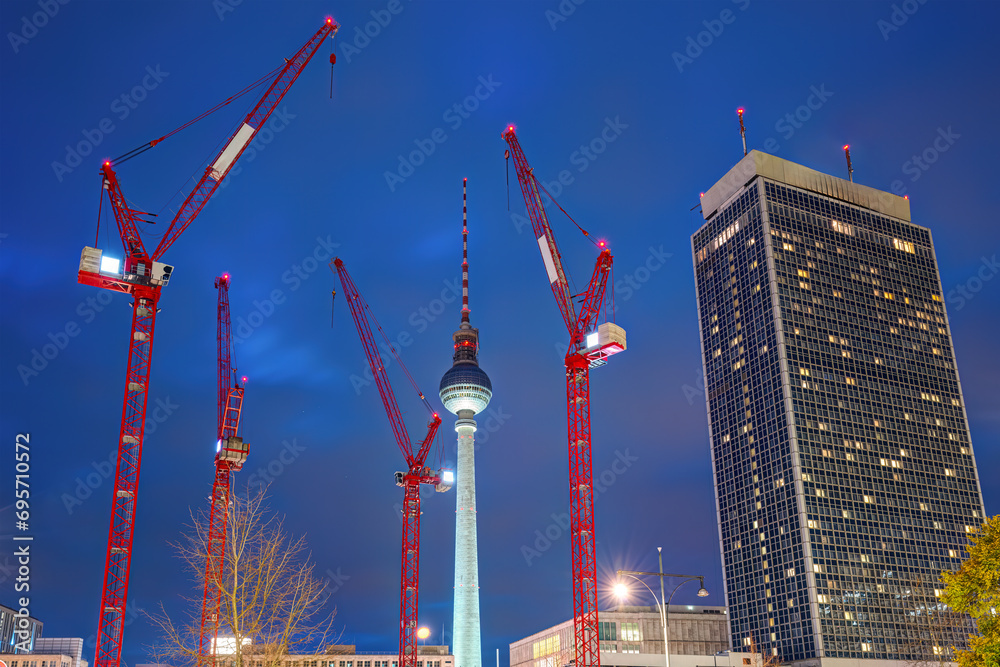 The famous Television Tower of Berlin at night with a skyscraper and four red construction cranes - obrazy, fototapety, plakaty 