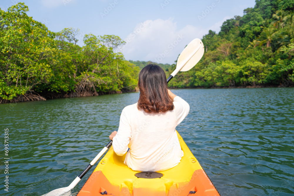 back view of woman kayaking In the green forest she does water sport activities.